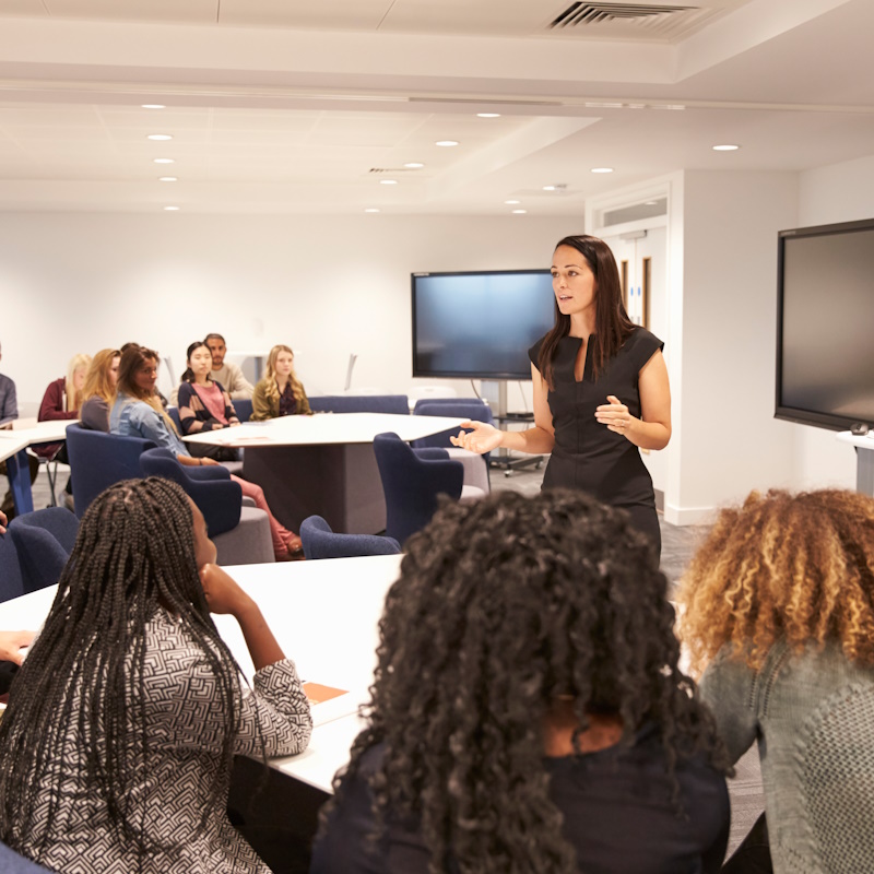 Femme présentant devant un groupe en salle de réunion.